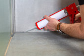 A plumber applies silicone sealant to the joining of ceramic tiles