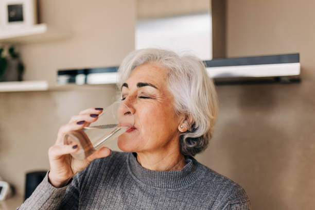 Elderly woman drinking fresh tap water at home Elderly woman drinking fresh tap water from a glass. Grey-haired mature woman staying healthy and hydrated at home. one mature woman only stock pictures, royalty-free photos & images