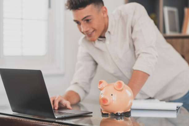 istock Man sit at desk manage expenses, calculate expenditures, pay bills online use laptop, makes household finances analysis, close up focus on pink piggy bank. Save money for future, be provident concept 1372301488