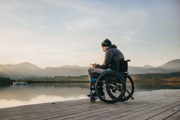 istock Disabled man in wheelchair using smart phone on pier by lake 1372302586