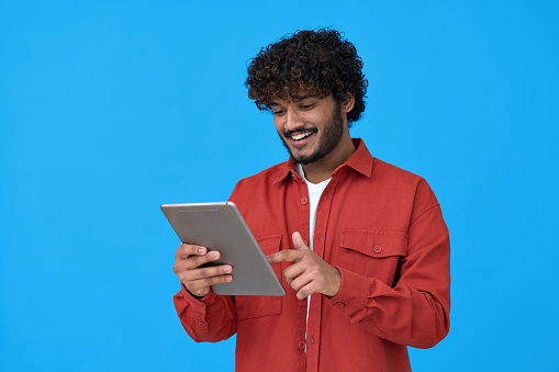 istock Happy indian guy using digital tablet isolated on blue background. 1372303816