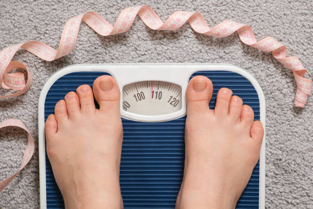 women's bare feet on floor scales and measuring tape, weight 100-110 kilograms, top view. the idea of obesity, weight loss and excess weight. - dieting overweight weight scale healthcare and medicine imagens e fotografias de stock