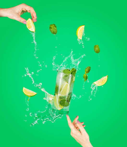 Woman hand support fly glass of tasty Mojito cocktail with lime and mint with splash, ingredients falling to glassful. stock photo