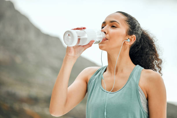 foto de una mujer joven tomando un descanso de hacer ejercicio para beber agua - agua potable fotos fotografías e imágenes de stock