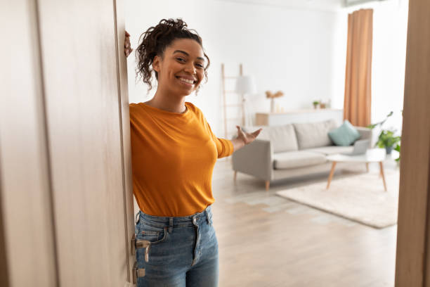 Cheerful African Woman Opening Door Welcoming You Standing At Home Cheerful African American Woman Opening Door And Gesturing Welcoming You To Come In Smiling To Camera Standing At Home. Hospitality, Real Estate Ownership And Purchase Concept domestic life stock pictures, royalty-free photos & images