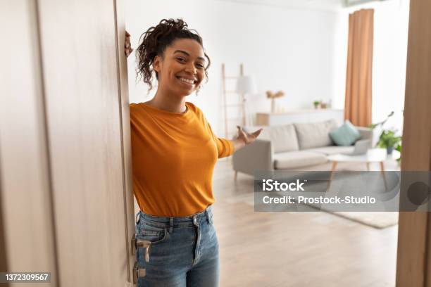 Cheerful African Woman Opening Door Welcoming You Standing At Home Stock Photo - Download Image Now