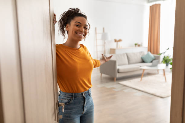 cheerful african woman opening door welcoming you standing at home - girmek stok fotoğraflar ve resimler