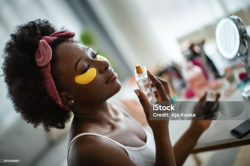It's time for my enjoyment and relaxation. Beautiful young woman with under eye patches, sitting and enjoying the scent of a beautiful perfume. Perfume Stock Photo