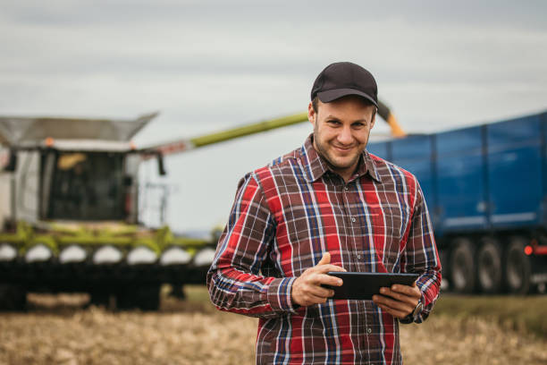 istock Farmer smiling at camera while holding a Tablet, standing on stubble field, combine Harvester in background 1372313659