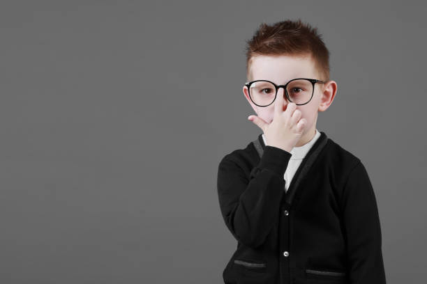 istock Smart child boy adjusts his glasses with finger on the grey background, close-up. Studio juvenile portrait in casual clothes. copy space 1372316487