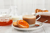 Traditional Italian Breakfast. Apricot Jam and Butter on Rusks or Fette Biscottate, toasted round Bread. Caffe lungo or morning coffee. Milk. White table and background. Copy space.