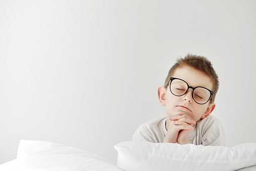 child boy in glasses praying in bedroom before going to bed. Empty space for text.