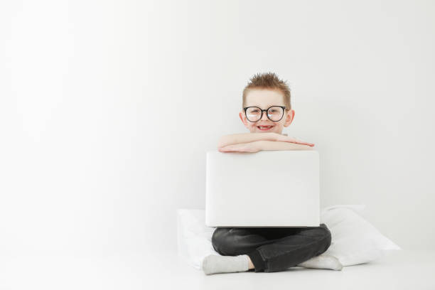 schoolboy in glasses using laptop sitting on bed. Child doing school homework and seriously and tired looking on camera.Online learning, distance lesson, education with online tutor at home isolation.