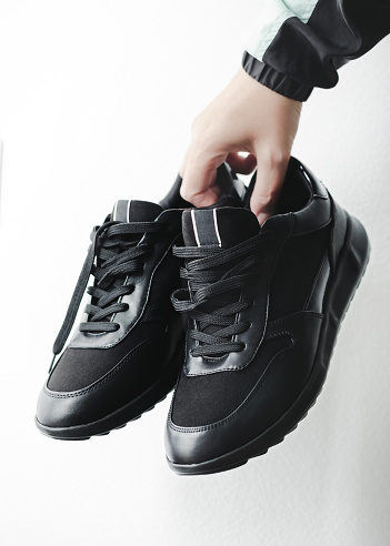 Hand holding black leather sneakers.