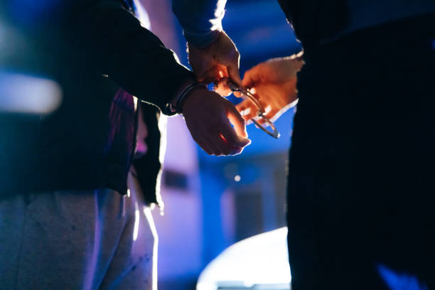 Policeman putting handcuffs on criminal's hands at night.
