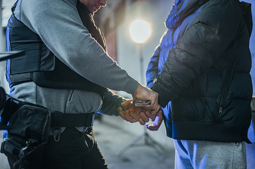 Police officer putting a handcuffs on criminal's hands in the evening.