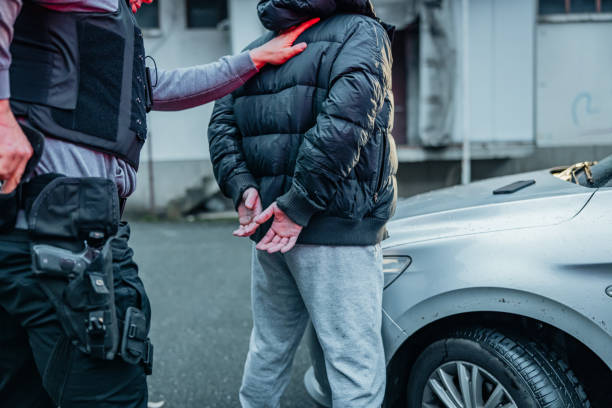 Police officer arresting a young gangster by the car stock photo