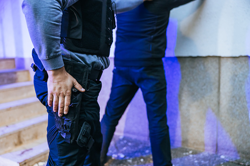 Task force officer reaching for a gun while arresting a suspect leaning on the wall.