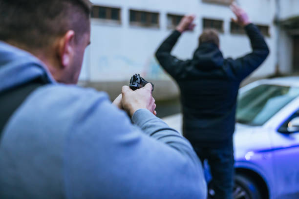 Policeman aiming a pistol to a surrendering suspect by the car.