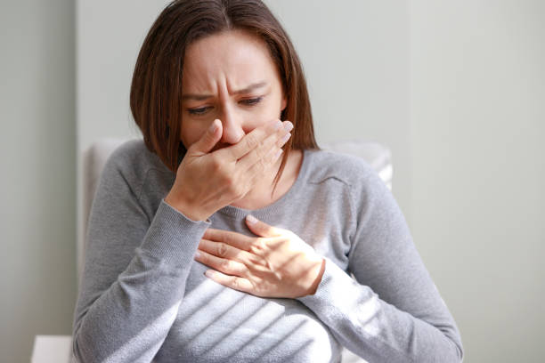 istock Young woman sitting alone on her sofa at home and coughing 1372323413