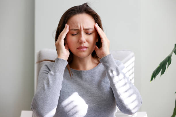 自宅での痛みのために不快感で頭を抱えている若い女性のショット - 頭痛 ストックフォトと画像