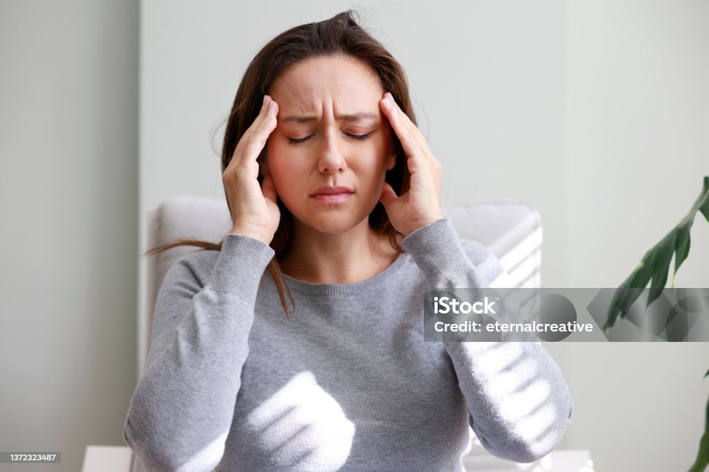 Shot of a young woman holding her head in discomfort due to pain at home Headache Stock Photo