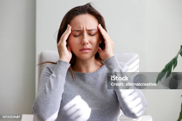 Shot Of A Young Woman Holding Her Head In Discomfort Due To Pain At Home Stock Photo - Download Image Now
