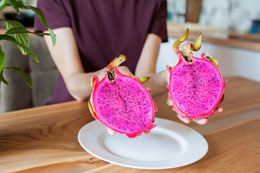 The girl holds in her hands a cut dragon fruit pitahaya at home in the kitchen close-up. soft focus