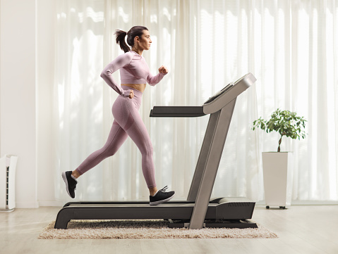 Full profile shot of a female in crop top and leggings running on a treadmill at home