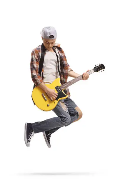 Photo of Male teenager jumping and playing an electric guitar