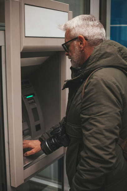 istock Mature man withdraws cash from an ATM, danger. Using a credit card while traveling. 1372325450