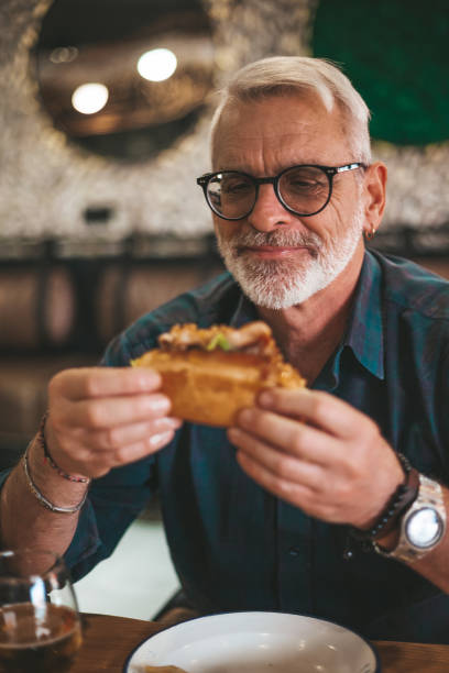 Hungry elderly man enjoying a delicious sandwich. Lunch break in a pub or restaurant.