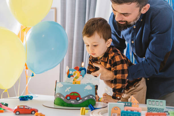 Father and son at home celebrating boys second birthday with cake and confetti.