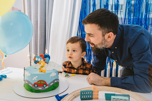 Father and son at home celebrating boys second birthday with cake and confetti.