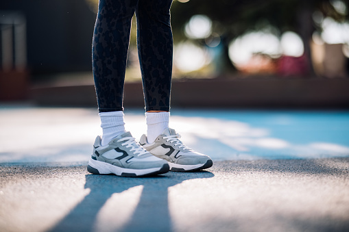 Side view of a lower body of an anonymous woman. She is wearing workout clothes: leggings, sneakers and socks. It's morning or later in the day. She might be preparing for her morning run.