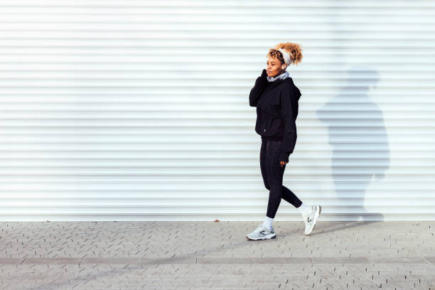 afroamerikanische frau, die mit ohrhörern neben dem weißen garagentor läuft - sports clothing jogging running 40s stock-fotos und bilder