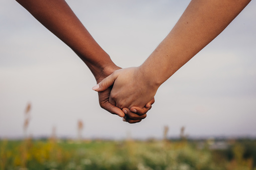 Close up of African and caucasian women holding hands on field on field during sunset