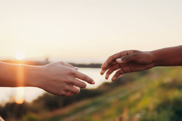 African and caucasian women reaching out their hands to each other African and caucasian women reaching out their hands to each other during sunset reaching stock pictures, royalty-free photos & images