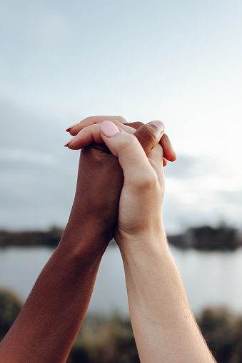 Close up of women holding hands with different skin colour against sky