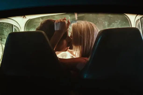 Young couple kissing each other while sitting inside vintage car at night