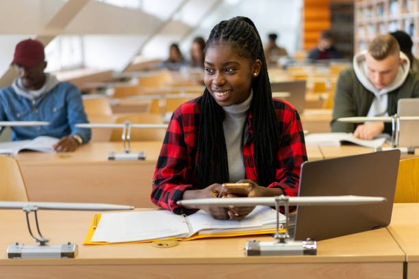 a smiling undergrad using her mobile during a lecture - multi ethnic group concentration mobile phone using laptop imagens e fotografias de stock