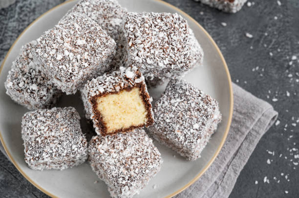 gâteau lamington australien traditionnel dans un glaçage au chocolat et des flocons de noix de coco sur une assiette sur fond de béton gris avec une tasse de thé. mise au point sélective. - lamingtons photos et images de collection