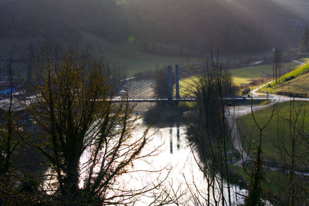 вид с воздуха на веревочный мост возле небольшого средневекового городка сен-урсанна с рекой ду и расфокусированными деревьями на передне� - doubs river стоковые фото и изображения