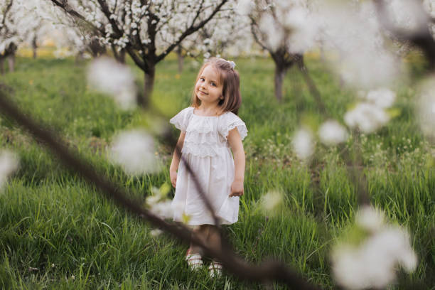 istock Female child in white dress posing under blooming apple tree 1372337972