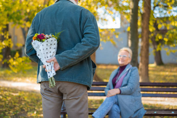 Senior man holding flowers behind his back stock photo