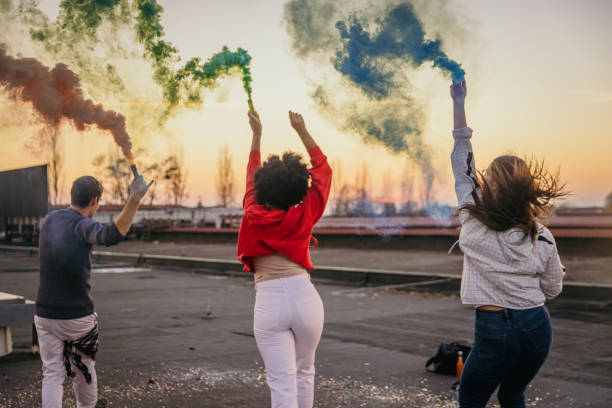 Young man and women holding multi colored smoke bombs on the rooftop