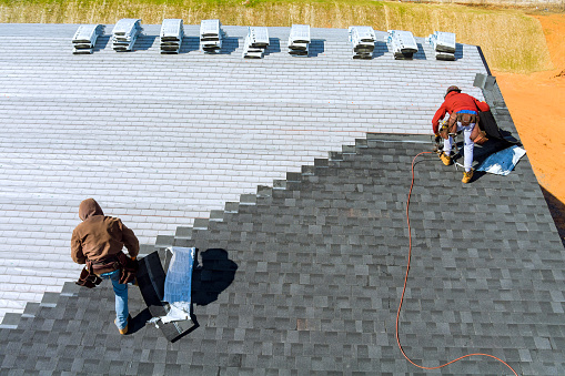 Manos de trabajadores instalando tejas de techo bituminosas con martillo neumático y clavo photo