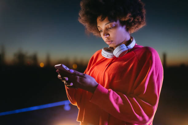 istock Young woman with headphones using mobile phone at night 1372341367