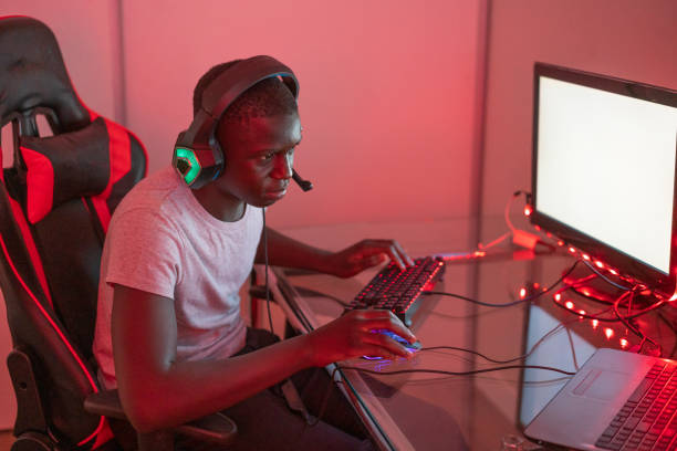 istock Young black male gamer playing at station using desktop computer and laptop 1372341640