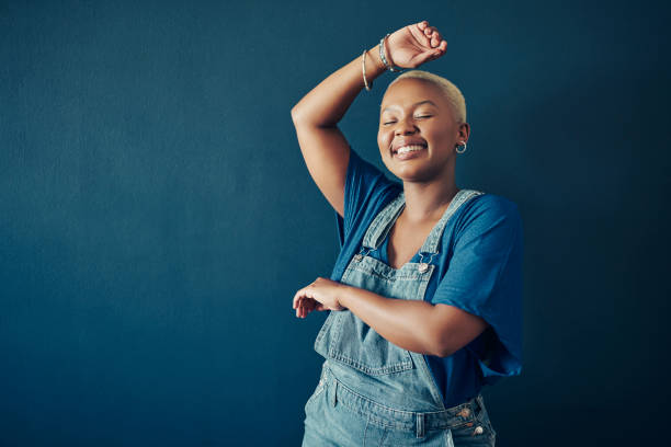 Smiling woman in blue overalls dancing against a blue background stock photo